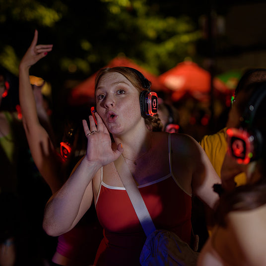 Quiet Events Silent Disco headphones for camps. A single girl wearing headphones with people and trees in the background.