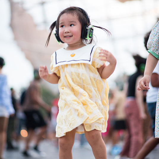 Quiet Events Silent Disco headphones for kids. A baby asian little girl having fun at the park with headphones.