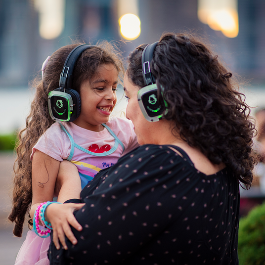 Quiet Events Silent Disco headphones for kids. A daughter and her mother looking at each other eyes enjoying and having fun with headphones.