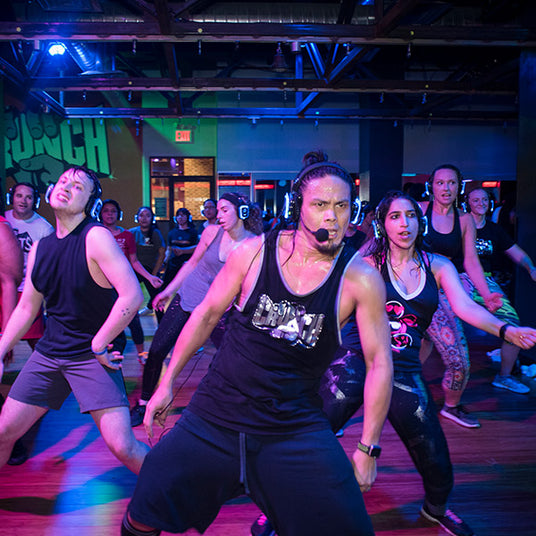 Quiet Events Silent Disco headphones for fitness and meditation. A gym instructor with a full dance class wearing headphones.