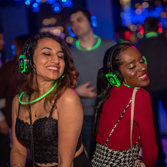 Quiet Events Silent Disco headphones for hotels. A pair of young women dancing and having fun on the dance floor with headphones.