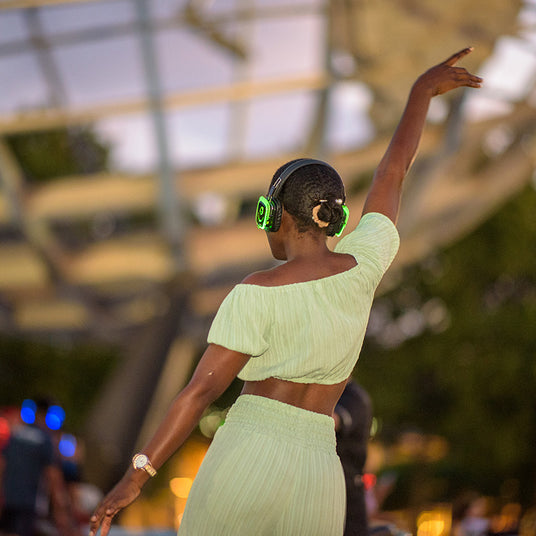 Quiet Events Silent Disco headphones for parks. A black female with her back dancing with one of her hand in the air.