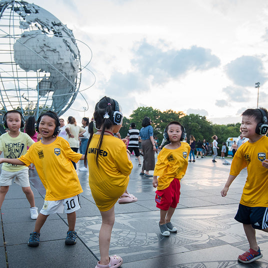 Quiet Events Silent Disco headphones for parks. A group of children playing and dancing together wearing headphones.