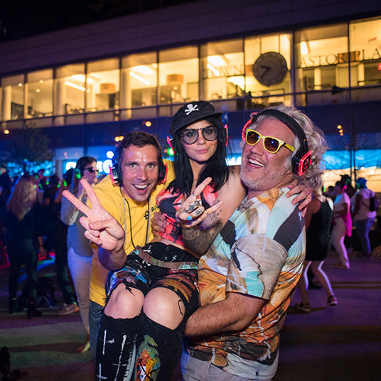 Quiet Events Silent Disco headphones for public spaces two guys carrying a girl in between them having fun and wearing headphones.