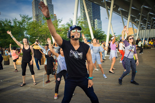 Quiet Events Silent Disco headphones for fitness.  An Instructor giving an aerobic class to others outdoors having fun wearing headphones.